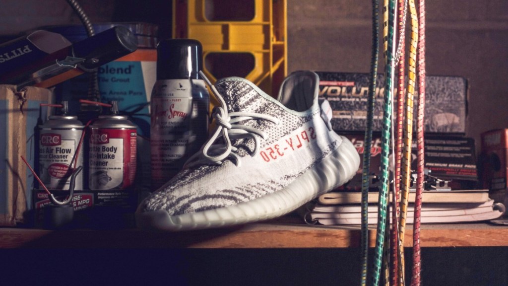 A garage shelf with spray cans, tie-down straps, books and a running shoe.