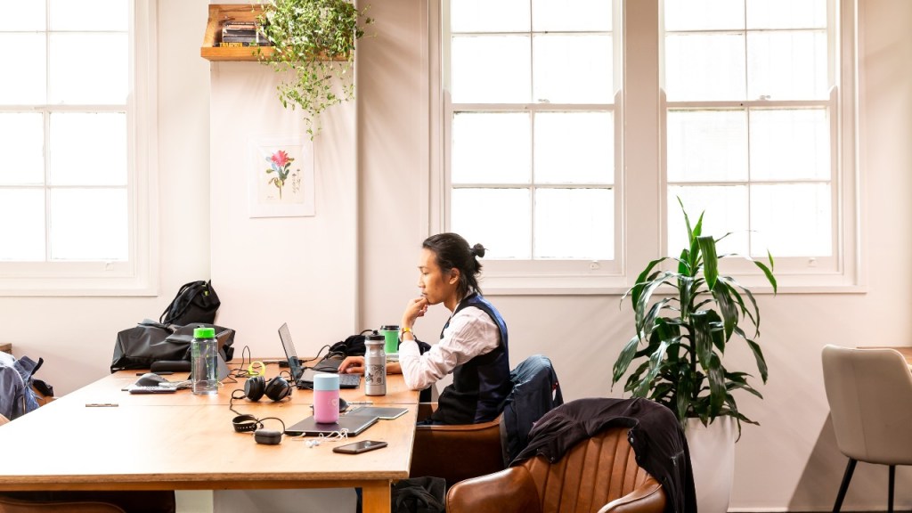Person sitting by window with laptop and other electronics at coworking space, Seed.